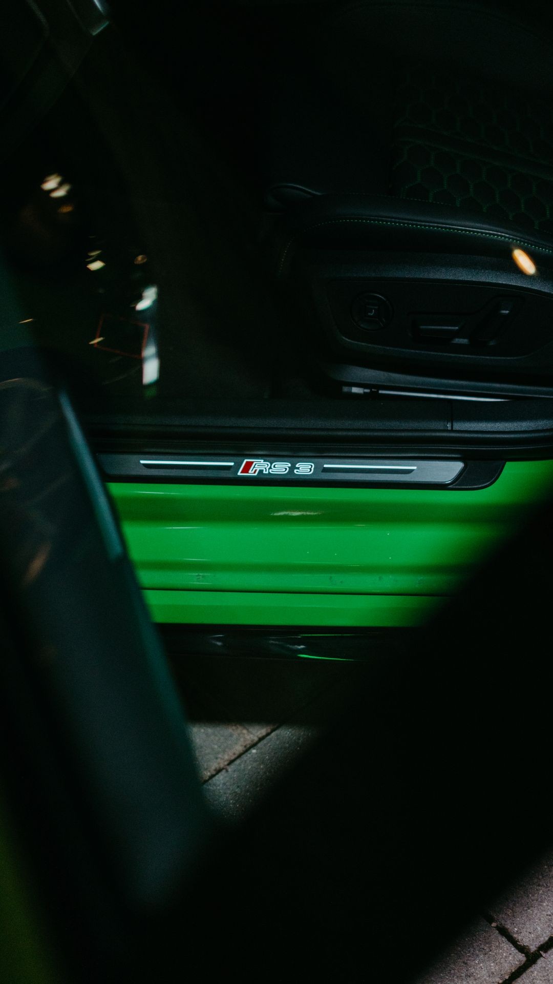 Close-up of a car's illuminated green door sill with 'RS 3' logo.