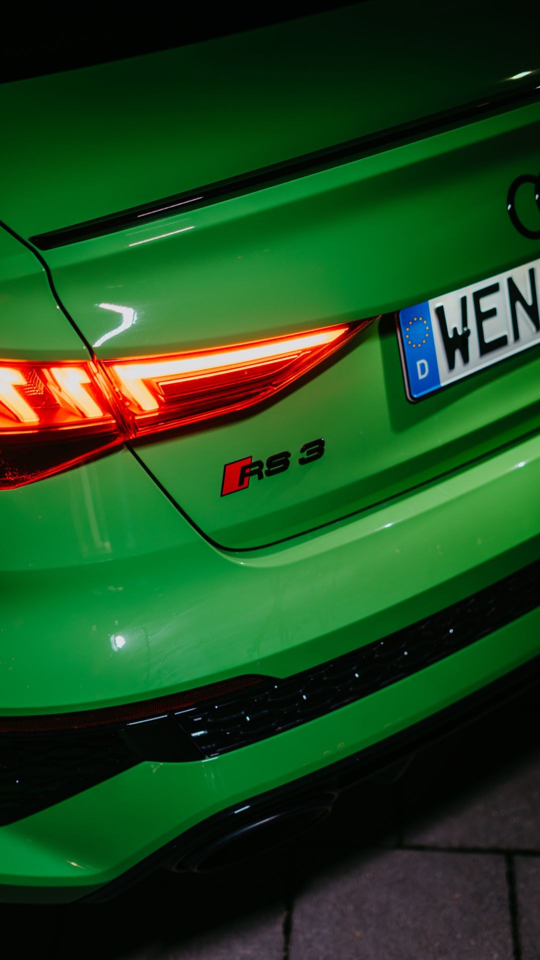 Close-up of a green car rear, showing RS 3 badge and taillights illuminated.