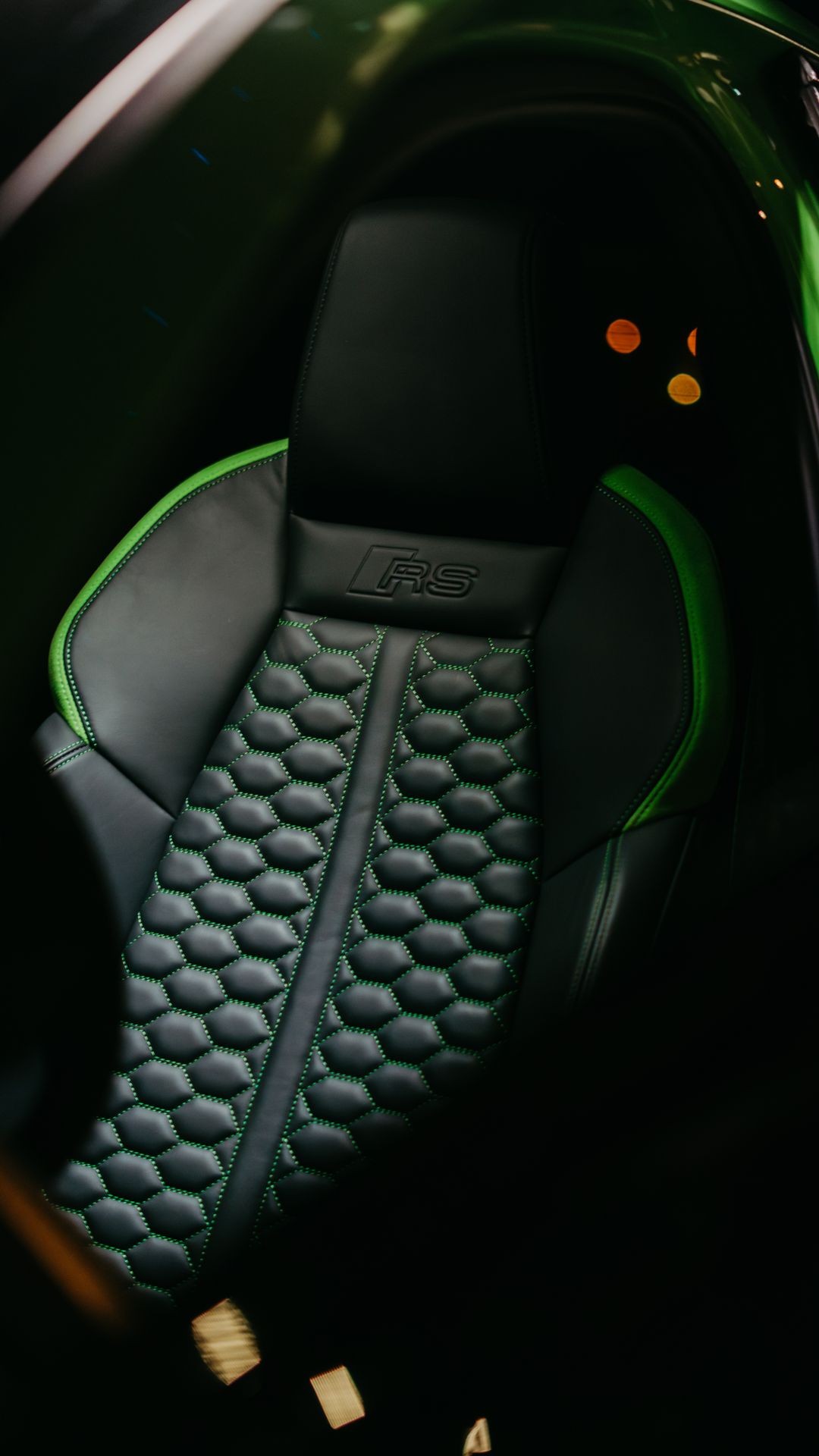 Close-up of a black leather car seat with green stitching and honeycomb pattern.